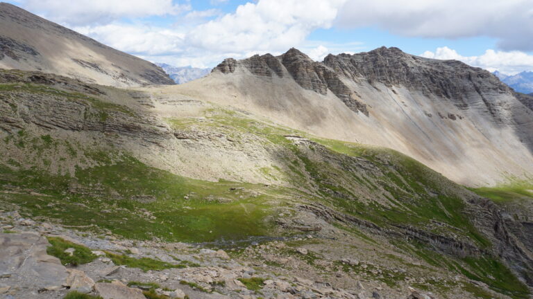 Vom Südostgrat geht es hinab in das grüne Tälchen, nach dem Fluss wieder hinauf zum Col de Rougnoux.