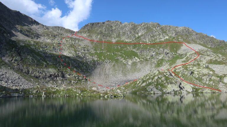 Blick vom Lai Blau Südufer zum Pass P. 2723. Gestrichelt die direkte Aufstiegsroute (Steinmännchen), durchgezogene Linie Variante Queurng auf Pfad, dann wegloser Abstieg zum See.