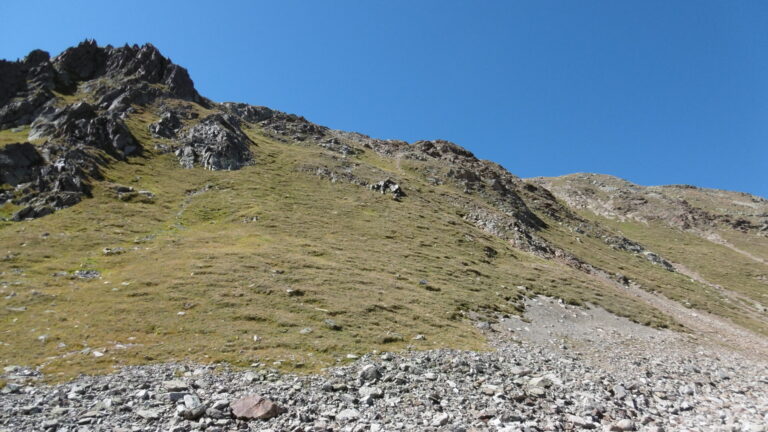 Auf dem Schuttfeld bei P. 2737. Über das diagonale Grasband steigt man zu dem Felskopf links.